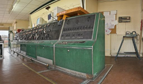 Vue d'ensemble de trois-quarts du poste électrique néoclassique à leviers d'itinéraires, combinateur mécanique type Alsthom et tableau de contrôle optique (T.C.O.).A sa droite établi pour la maintenance du service électrique. © Région Bourgogne-Franche-Comté, Inventaire du patrimoine