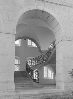 Départ du grand escalier vu à travers une arcade de la galerie bordant la cour. © Région Bourgogne-Franche-Comté, Inventaire du patrimoine