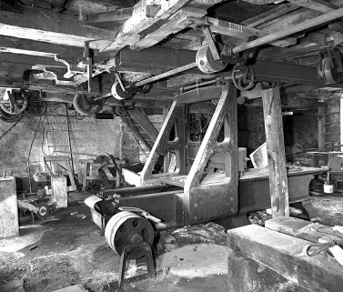 Partie arrière : poulies et engrenages d'entraînement de la table. En côté de l'entretoise, manivelle de réglage en hauteur de la traverse porte-outil. © Région Bourgogne-Franche-Comté, Inventaire du patrimoine