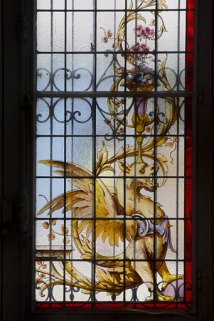 Intérieur, vitrail dans une fenêtre du rez-de-chaussée : détail du motif gauche représentant un dragon ailé. © Région Bourgogne-Franche-Comté, Inventaire du Patrimoine
