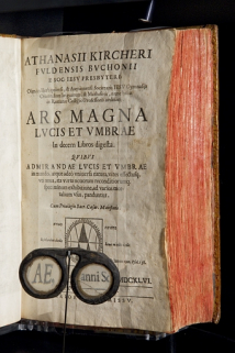 Besicles devant le traité sur la lumière " Ars magna lucis et umbrae ". Traité d'Athanase Kircher, édité en 1646. Collection du musée de la Lunette, Morez. © Région Bourgogne-Franche-Comté, Inventaire du patrimoine Besicles devant le traité sur la lumière " Ars magna lucis et umbrae ". Traité d'Athanase Kircher, édité en 1646. Collection du musée de la Lunette, Morez. © Région Bourgogne-Franche-Comté, Inventaire du patrimoine