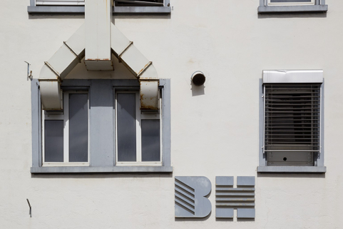 Usine, 1er corps de bâtiment : fenêtre horlogère et logotype, sur la façade latérale gauche. © Région Bourgogne-Franche-Comté, Inventaire du patrimoine Usine, 1er corps de bâtiment : fenêtre horlogère et logotype, sur la façade latérale gauche. © Région Bourgogne-Franche-Comté, Inventaire du patrimoine