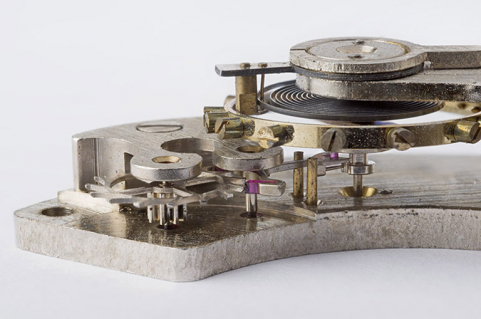 L'échappement : vue plongeante de profil. De gauche à droite : roue d'ancre et son pignon, l'ancre, le balancier-spiral avec son plateau (dessous) et la raquette (dessus, modifiant la longueur active du spiral). © Région Bourgogne-Franche-Comté, Inventaire du patrimoine