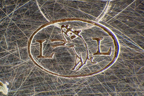 Poinçon d'importateur de la fabrique Louis Lang SA (deux L encadrant un cochon debout), insculpé dans le fond. © Région Bourgogne-Franche-Comté, Inventaire du patrimoine