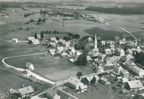 Le Russey (Doubs). 22180 - Vue panoramique aérienne [le village vu de l'ouest], milieu 20e siècle. Le bâtiment est visible à gauche, derrière la gare. © Région Bourgogne-Franche-Comté, Inventaire du patrimoine