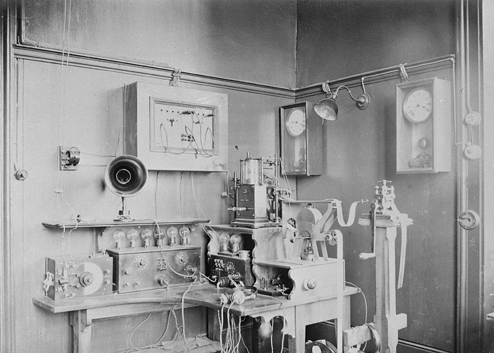 [Installation pour la transmission électrique de l'heure], 1ère moitié 20e siècle. On reconnaît sur la table le chronographe Boulitte, relié à l'appareil à réservoir et au module d'entraînement du papier, posé sur un socle en hauteur (à droite). © Région Bourgogne-Franche-Comté, Inventaire du patrimoine