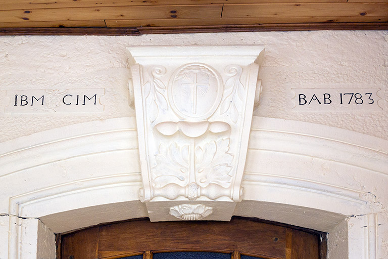 Façade sud : arc monolithe en béton avec sa fausse clef de voûte, des initiales et un chronogramme. © Région Bourgogne-Franche-Comté, Inventaire du patrimoine