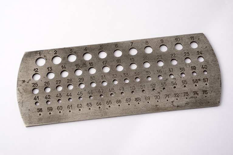Calibre (ou jauge) à trous (12 x 5 cm, h = 2 mm), destiné à mesurer des diamètres et percé de 75 trous de diamètre décroissant, numérotés de 1 (le plus grand) à 75 (le plus petit). © Région Bourgogne-Franche-Comté, Inventaire du patrimoine