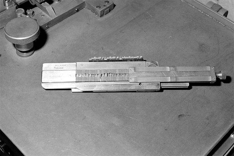 Face inférieure du composteur permettant le centrage des caractères sur la ligne. Le caractère apparaît en négatif dans chaque matrice ; la ligne-bloc fondue est placée à côté du composteur. © Jérôme Mongreville / Région Bourgogne-Franche-Comté, Inventaire du patrimoine - 2001