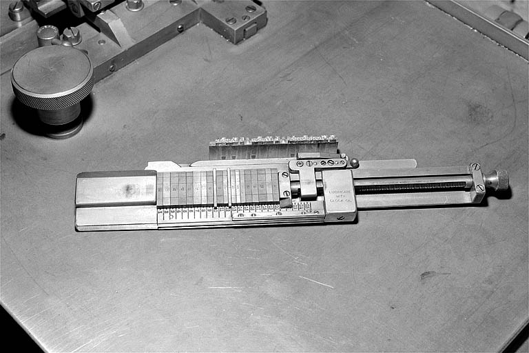 Face supérieure du composteur permettant le centrage des caractères sur la ligne. Le caractère apparaît au recto de chaque matrice ; la ligne-bloc fondue est placée à côté du composteur. © Jérôme Mongreville / Région Bourgogne-Franche-Comté, Inventaire du patrimoine - 2001