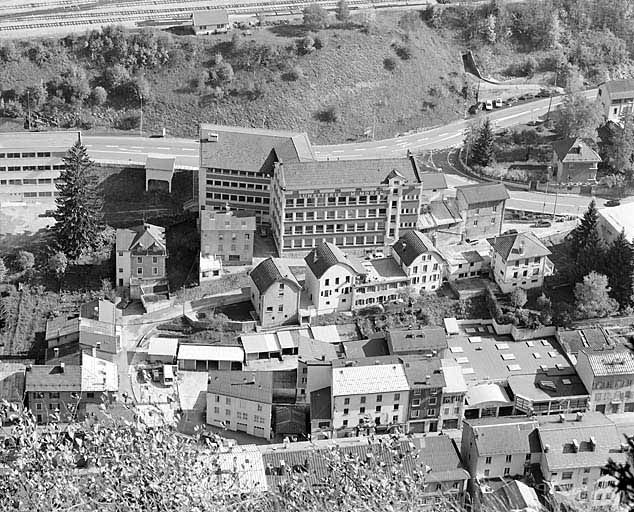 Anciennes usines de lunetterie Marius Morel (18 à 22 avenue Charles de Gaulle) et Cok et Cie (8 à 12 rue de la Paix). L'usine Cok était composée des deux maisons coiffées d'un toit en carène (au centre) et de l'atelier qui les réunit. © Yves Sancey / Région Bourgogne-Franche-Comté, Inventaire du patrimoine - 2003 Anciennes usines de lunetterie Marius Morel (18 à 22 avenue Charles de Gaulle) et Cok et Cie (8 à 12 rue de la Paix). L'usine Cok était composée des deux maisons coiffées d'un toit en carène (au centre) et de l'atelier qui les réunit. © Yves Sancey / Région Bourgogne-Franche-Comté, Inventaire du patrimoine - 2003