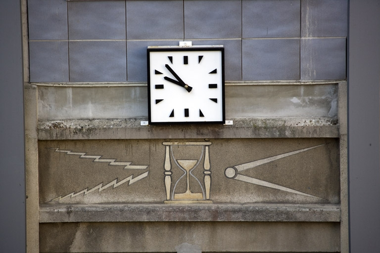 Traverse : horloge et décor marquant l'axe central (vue rapprochée). Le sablier symbolise l'horlogerie, les éclairs l'électricité et le compas la mécanique. © Yves Sancey / Région Bourgogne-Franche-Comté, Inventaire du patrimoine - 2009 Traverse : horloge et décor marquant l'axe central (vue rapprochée). Le sablier symbolise l'horlogerie, les éclairs l'électricité et le compas la mécanique. © Yves Sancey / Région Bourgogne-Franche-Comté, Inventaire du patrimoine - 2009