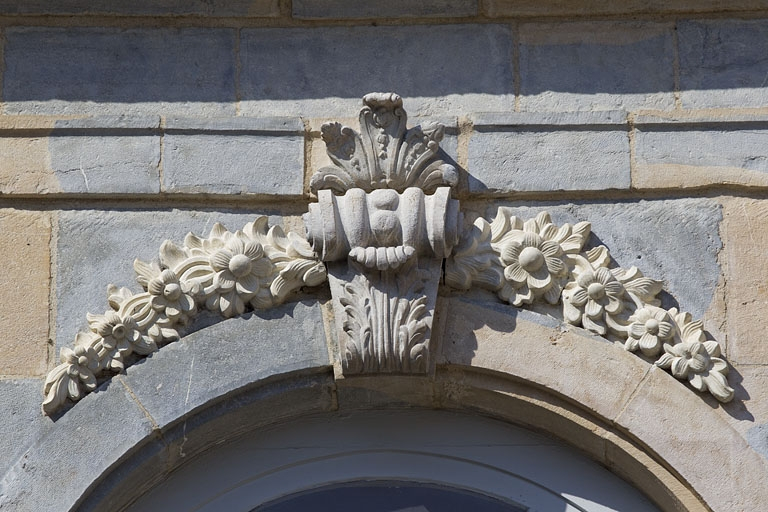Façade en fond de cour, avant-corps central, fenêtre du premier étage : clé de l'arc, détail du décor feuillagé encadré de deux guirlandes de fleurs. © Yves Sancey / Région Bourgogne-Franche-Comté, Inventaire du patrimoine - 2010