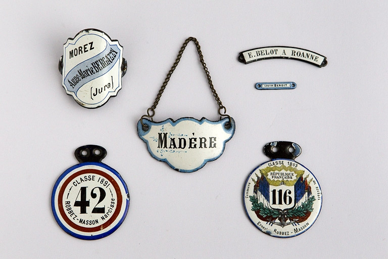 Exemple de production émaillée : plaques d'identification. Plaque de vélo (en haut à gauche), de parapluie (Benoît, à droite), jetons de conscrits, etc. © Yves Sancey / Région Bourgogne-Franche-Comté, Inventaire du patrimoine - 2010