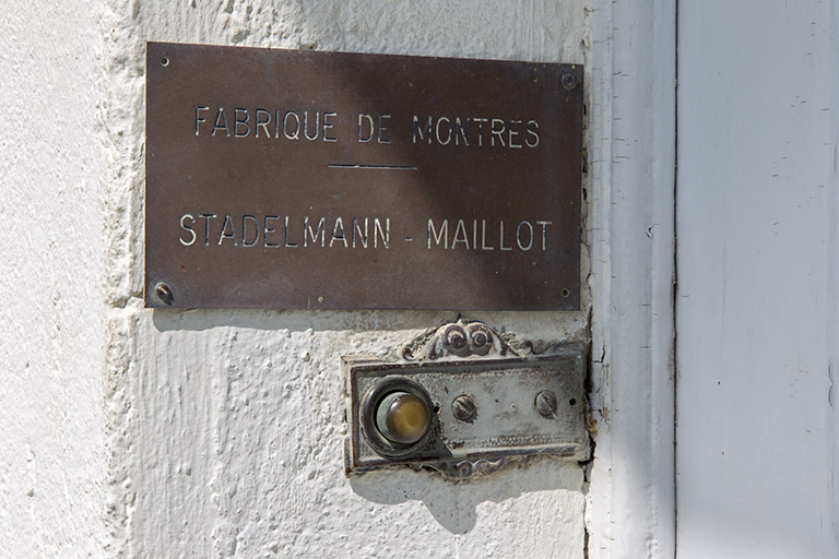 Façade latérale gauche : plaque de la fabrique de montres Stadelmann-Maillot, à l'entrée. © Sonia Dourlot / Région Bourgogne-Franche-Comté, Inventaire du patrimoine - 2014