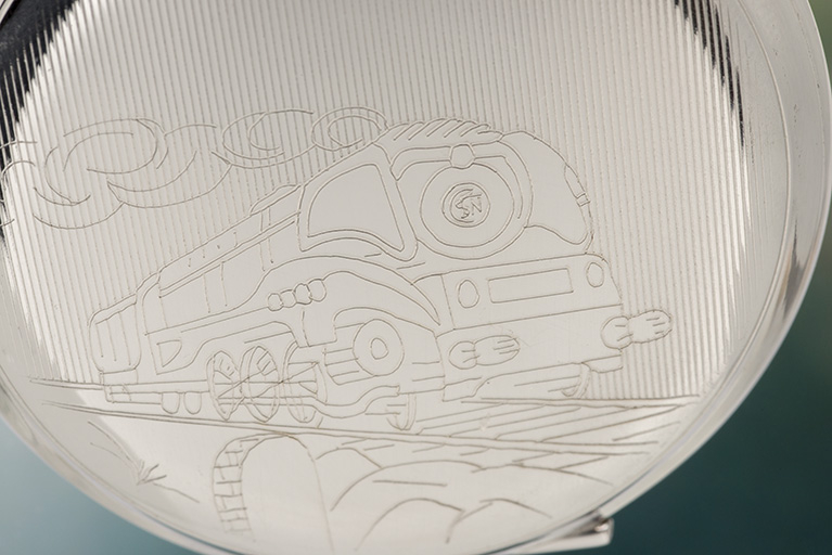 Boîte de montre de gousset en métal chromé : détail du décor montrant une locomotive à vapeur (un modèle 232 U). © Sonia Dourlot / Région Bourgogne-Franche-Comté, Inventaire du patrimoine - 2015