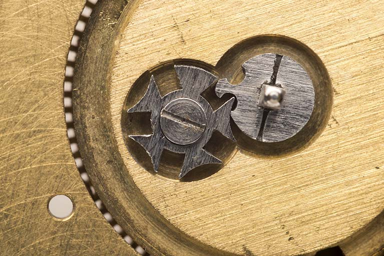 Platine nue, côté cadran : le système d'arrêtage du barillet (croix de Malte), pemettant de limiter le degré d'armage du ressort moteur. © Sonia Dourlot / Région Bourgogne-Franche-Comté, Inventaire du patrimoine - 2015