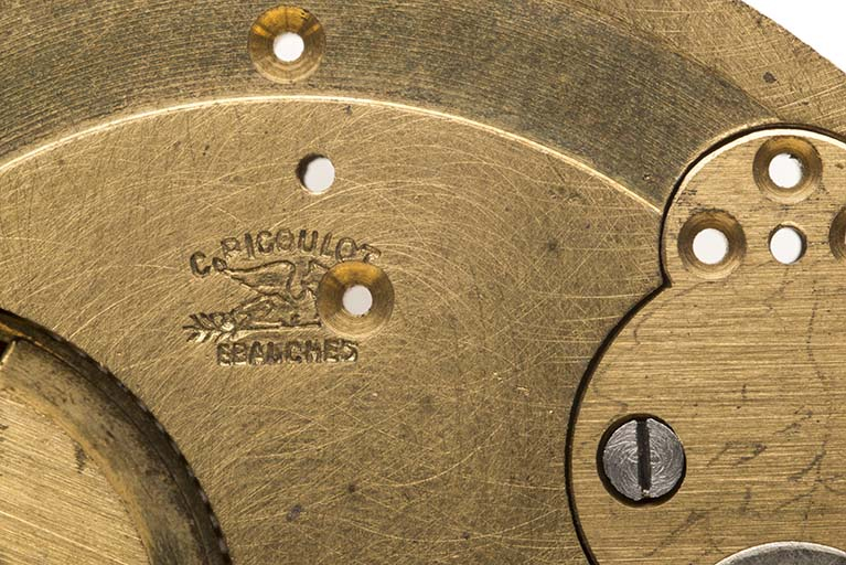 Platine nue, côté cadran : marque du fabricant avec inscription (C. Picoulot / Ebauches) et griffon couché sur une flèche. © Sonia Dourlot / Région Bourgogne-Franche-Comté, Inventaire du patrimoine - 2015