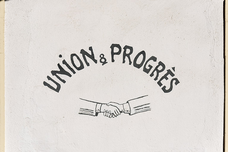 Devise Union et Progrès et poignée de main, peintes sur la façade antérieure. © Sonia Dourlot / Région Bourgogne-Franche-Comté, Inventaire du patrimoine - 2017 Devise Union et Progrès et poignée de main, peintes sur la façade antérieure. © Sonia Dourlot / Région Bourgogne-Franche-Comté, Inventaire du patrimoine - 2017
