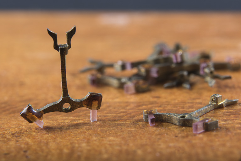 Ancres de montre (collection Jean-Claude Vuez, Villers-le-Lac). Celle placée verticalement repose sur ses deux palettes en rubis et présente sa fourchette en partie haute. Le paquet porte l'inscription : "10 fourchettes / 18'' [...] / vis sans fin". © Sonia Dourlot / Région Bourgogne-Franche-Comté, Inventaire du patrimoine - 2018